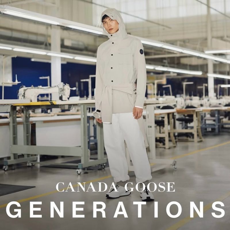 A person standing in a bright factory wearing a light gray hooded jacket, and white pants, showcasing a modern, clean aesthetic in an industrial setting.