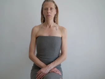 Model wearing a strapless grey dress and long crystal earrings against a plain grey backdrop for Rier Winter 2025.