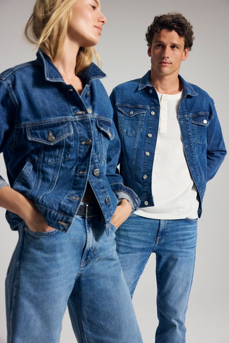 Denim-clad couple in matching jackets and jeans against a neutral background. Stylish fashion portrait showcasing denim fashion.