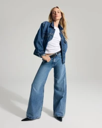 Model in denim jacket and wide-leg jeans standing against a light grey studio background.