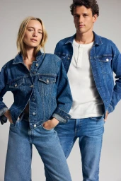 Two models wearing matching blue denim jackets and jeans against a neutral grey studio background for Mavi FW25 campaign.