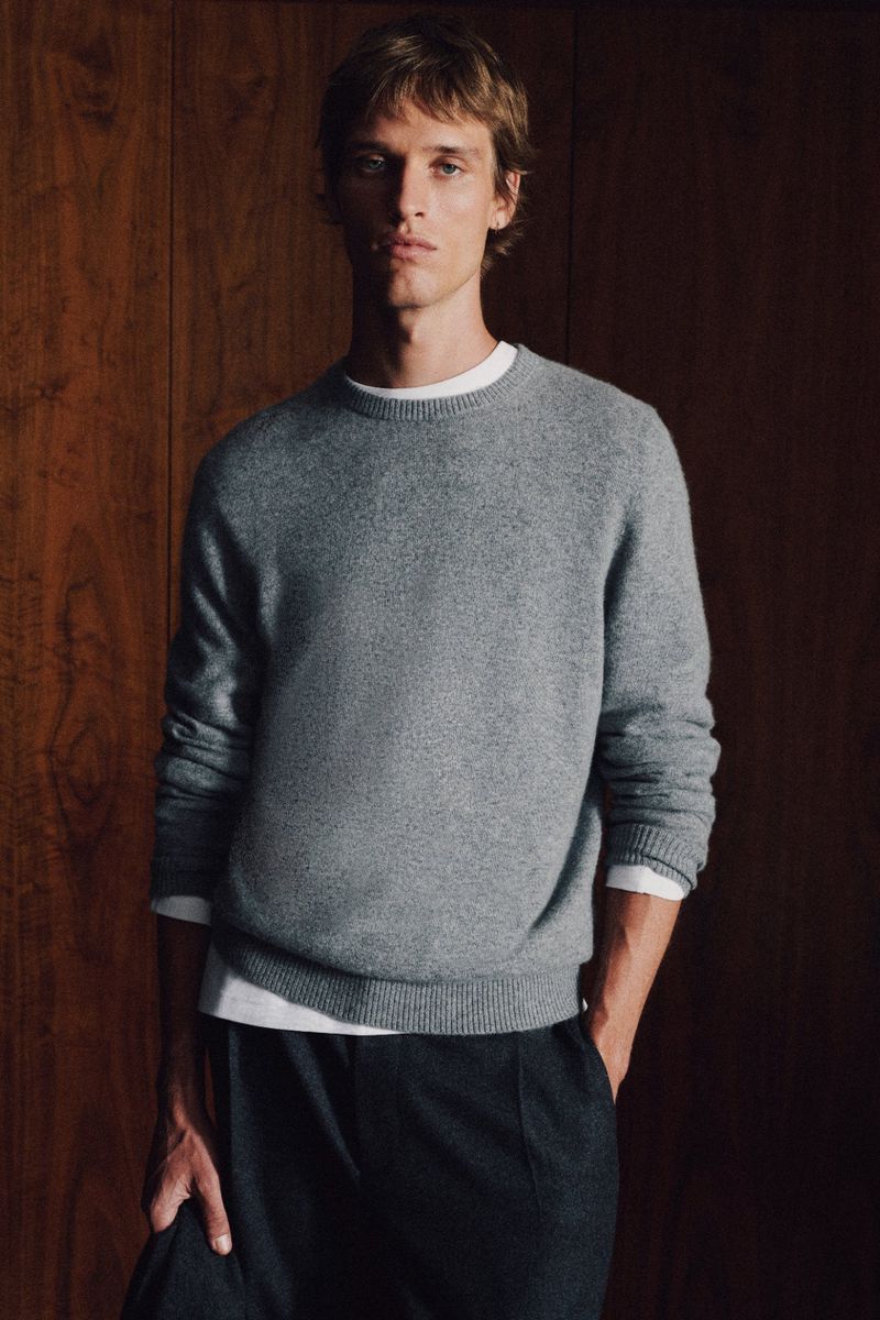 Portrait of a handsome adult male wearing a gray sweater against a brown wood panel background in eye-level medium studio shot.
