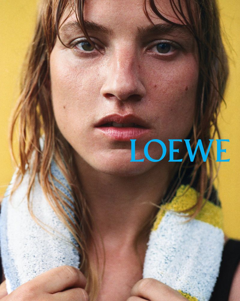 Close-up of a young fair-skinned adult female model with damp, light brown hair and a white, yellow, and blue towel around her neck.