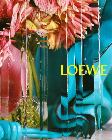 Floral arrangement featuring pink and yellow gerbera daisies in a vase with a blue jacket, set against a layered, cut-paper background.