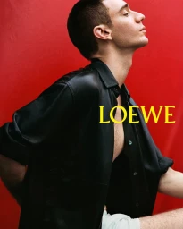 Man wearing a black leather shirt looking upward against a vibrant solid red background with yellow typography
