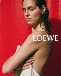 Model with wet hair holding a white towel against a vibrant red background in a campaign image for Loewe