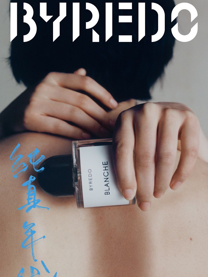 Close-up of a woman's back and arms, holding a Byredo Blanche perfume bottle, with brand logo and Chinese script visible.
