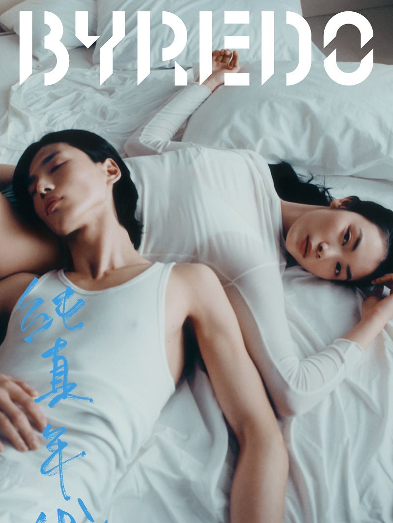 Two people lie on a bed with white linens. A woman and a man wear white. “Byredo” logo and Chinese characters are visible.