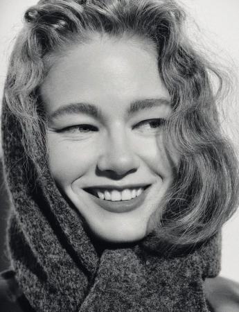 Close-up portrait of a smiling woman with curly hair wearing a dark-colored, textured headscarf in a black and white photo.