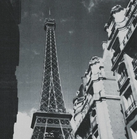 Low-angle shot of the Eiffel Tower in Paris, France, framed by classic urban architecture, in black and white with a cloudy sky.