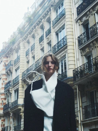 Woman in oversized blazer and draped white shirt posing in front of classic architecture, overcast daylight, medium shot.