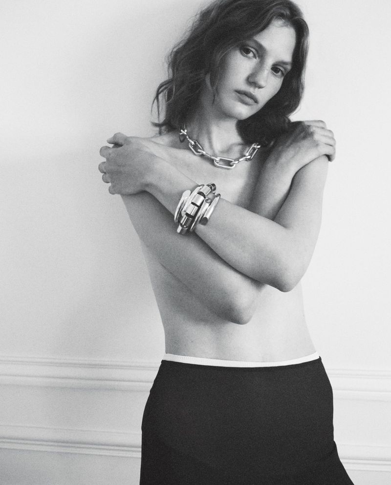 Black and white portrait of a female fashion model wearing a silver chain necklace and bracelet against a neutral background.