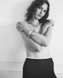Model Nadine Kirilova wearing chunky silver jewelry and dark skirt against plain wall