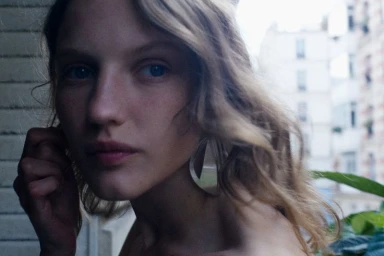 Close-up portrait of a woman with light brown hair wearing large drop earrings against an urban background.
