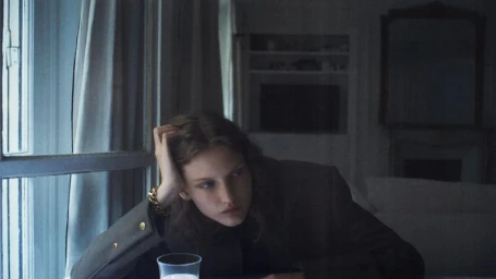 Model resting head on hand near window in dim interior for Vogue Thailand editorial