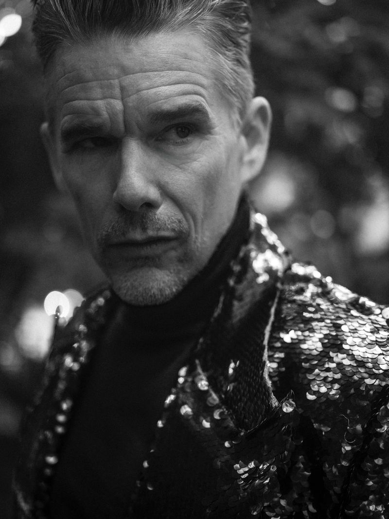 Monochrome portrait of adult male wearing sequined jacket, posed outdoors with shallow depth of field. Editorial fashion photograph.