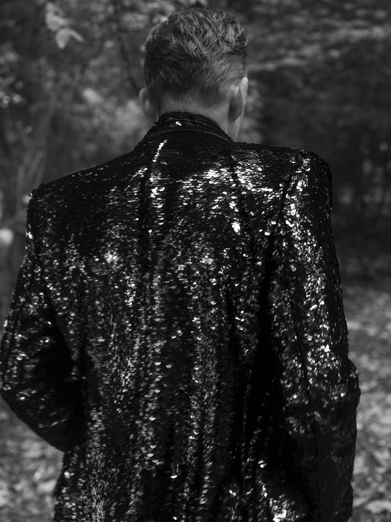 Actor Ethan Hawke seen from behind wearing a shimmering black sequin jacket outdoors in a monochrome portrait.