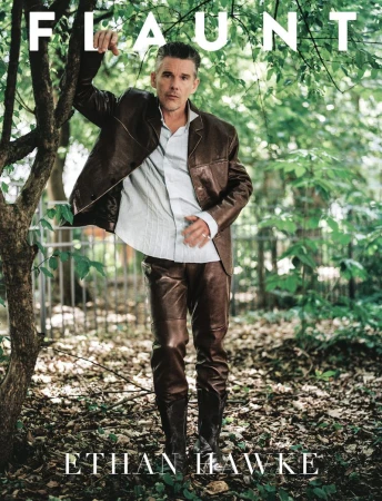 Ethan Hawke poses in a brown leather jacket and pants against a leafy outdoor background for a magazine cover, creating a stylish portrait.