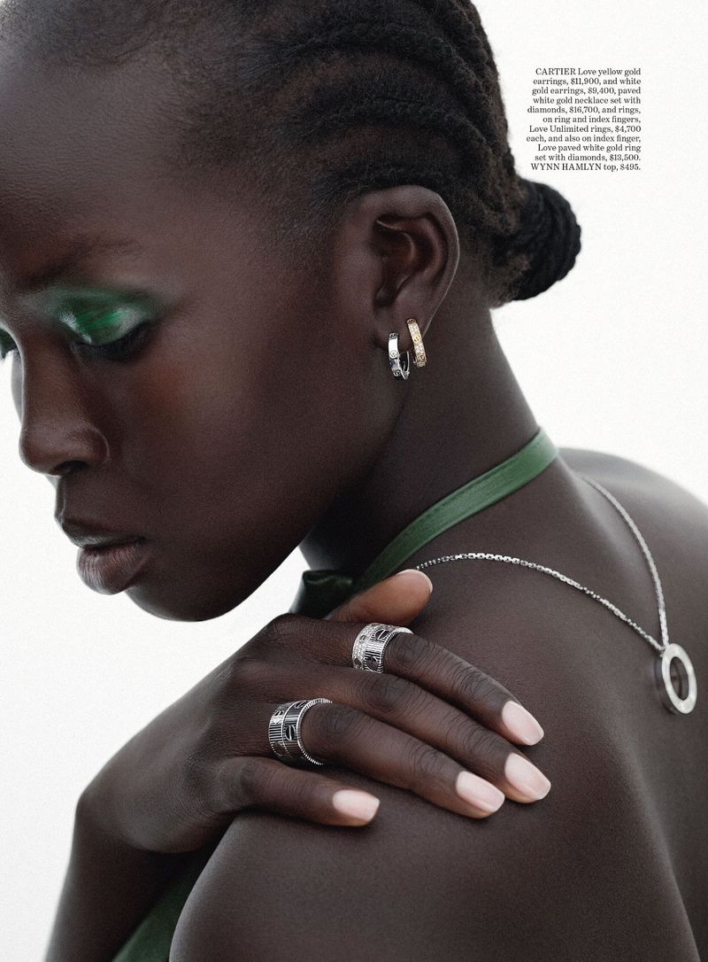 Close-up portrait of a dark-skinned woman wearing jewelry, including hoop earrings and rings. She is wearing green eye shadow.
