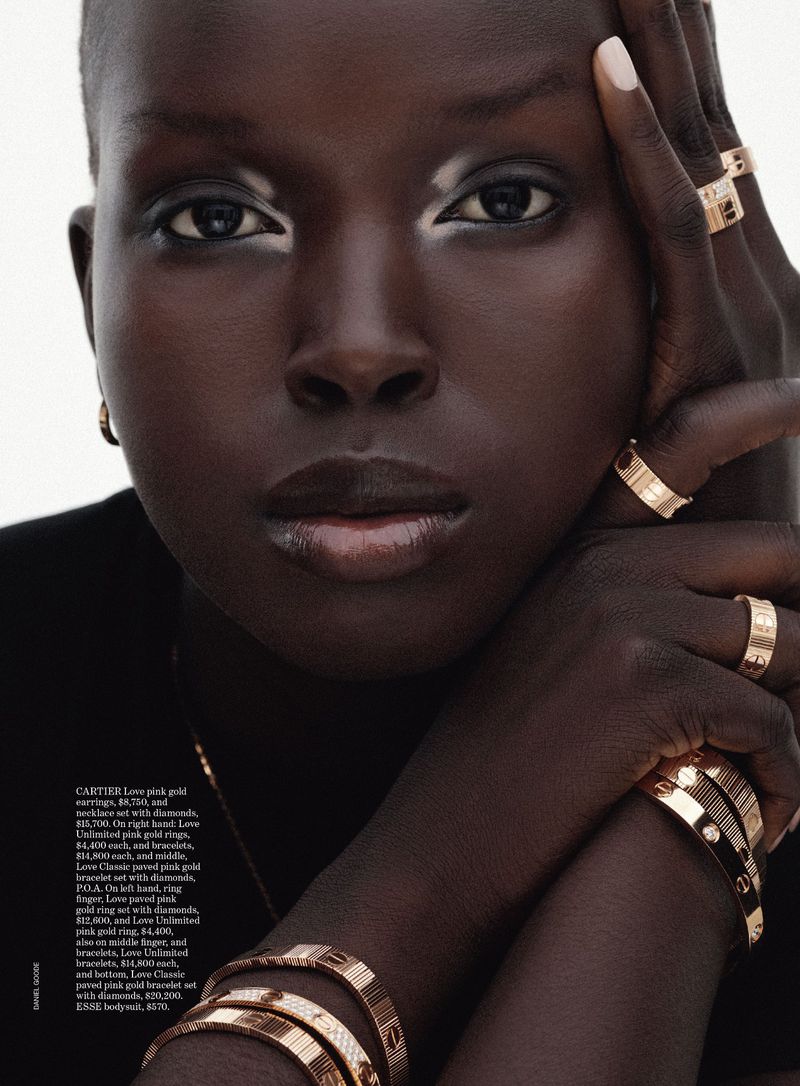 Close-up beauty shot of a dark-skinned adult woman adorned with gold Cartier rings and bracelets, white eye makeup, and neutral nails.