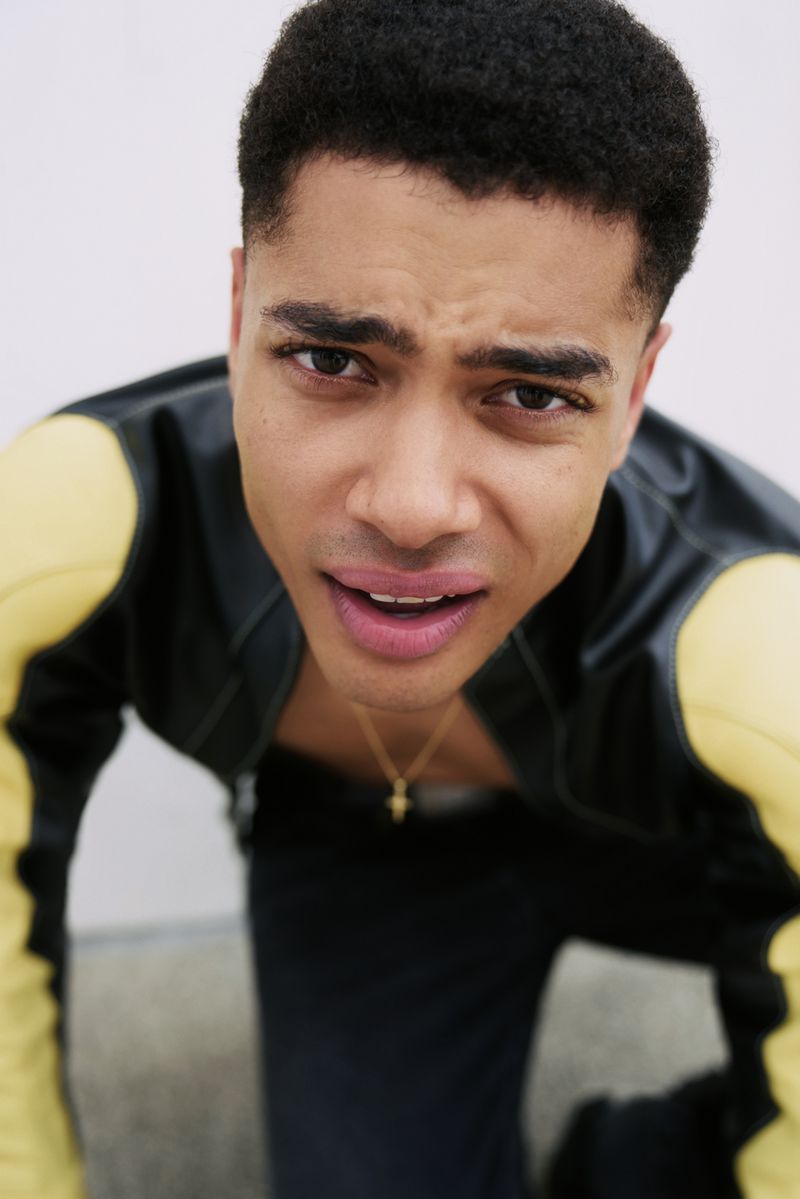 Close-up portrait of a young adult male with a slight frown, wearing a black and yellow jacket, looking directly at the camera.