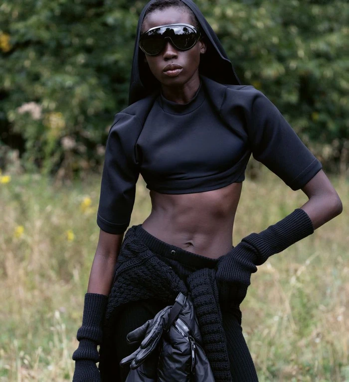 Model wearing dark futuristic sunglasses and black cropped top outdoors with a blurred natural background