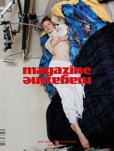 Model lying on a bed draped in blue and plaid blankets wearing a cream sweater and white skirt for magazinemagazine