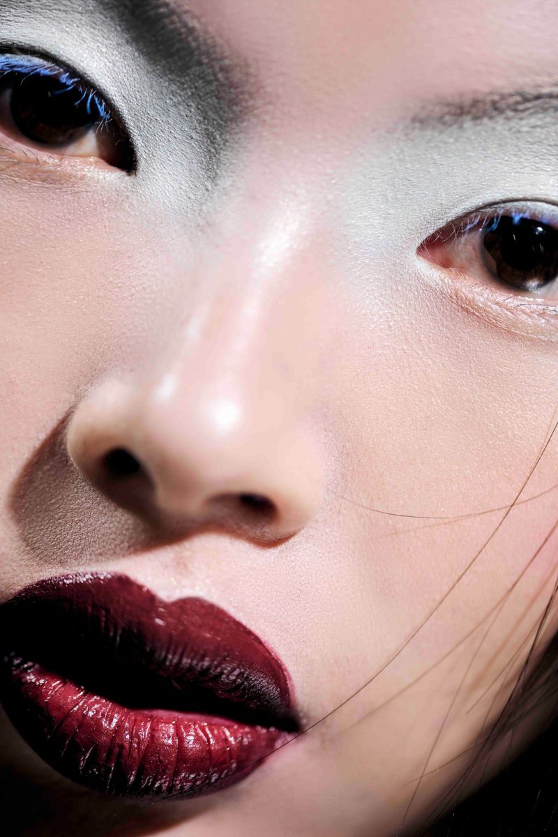 Close-up beauty portrait of model He Zhi wearing glossy dark burgundy lipstick and pale frosted eyeshadow for Mirror Mirror Magazine.