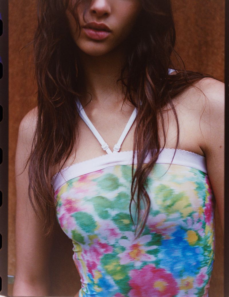 Portrait of a woman with long brown hair wearing a floral top with white straps against a blurred brown background.