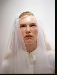 Close-up portrait of female model Astrid Østergaard wearing a sheer veil and white shirt against a neutral background.