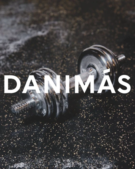 Close-up of a dumbbell resting on a dark, speckled surface with a dusting of white powder and the text 'DANIMÁS' in white.