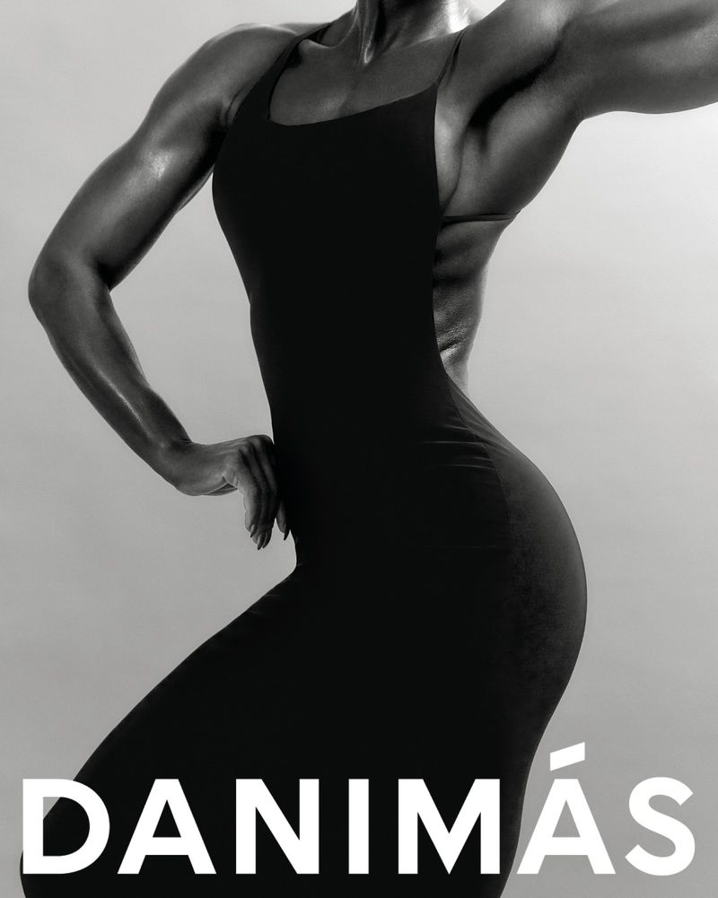 Monochrome portrait of a muscular woman in a black form-fitting dress against a solid background, highlighting strength and fashion.