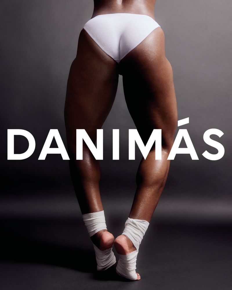 Lower half of a muscular woman in underwear, standing with wrapped ankles, lit from above against a dark gray studio backdrop.