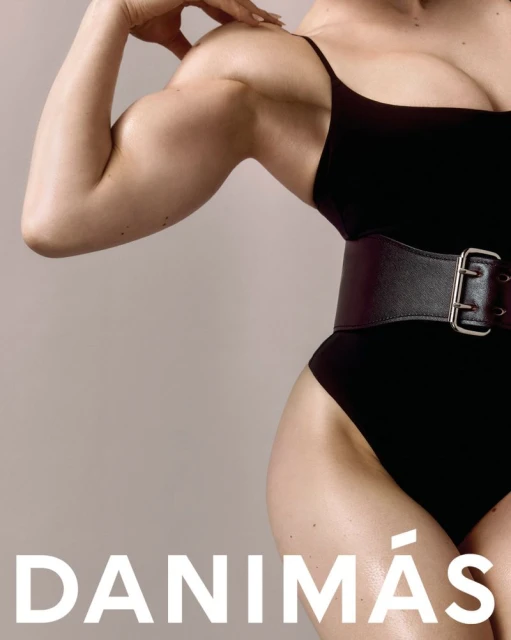 Strong woman flexing bicep wearing a black swimsuit with a belt in a studio setting, fitness and fashion concept. 
