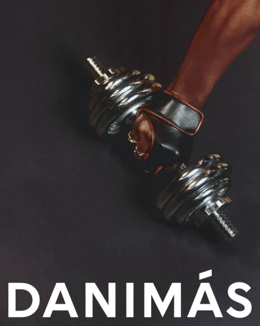 A gloved hand holds a chrome dumbbell against a dark backdrop. The image promotes fitness with a weight and brand name.