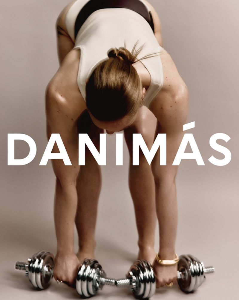 A woman in athletic wear bending over with a dumbbell in each hand, against a solid neutral studio background with the text DANIMÁS.