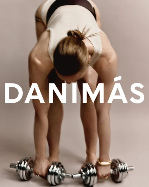 A woman in athletic wear bending over with a dumbbell in each hand, against a solid neutral studio background with the text DANIMÁS.