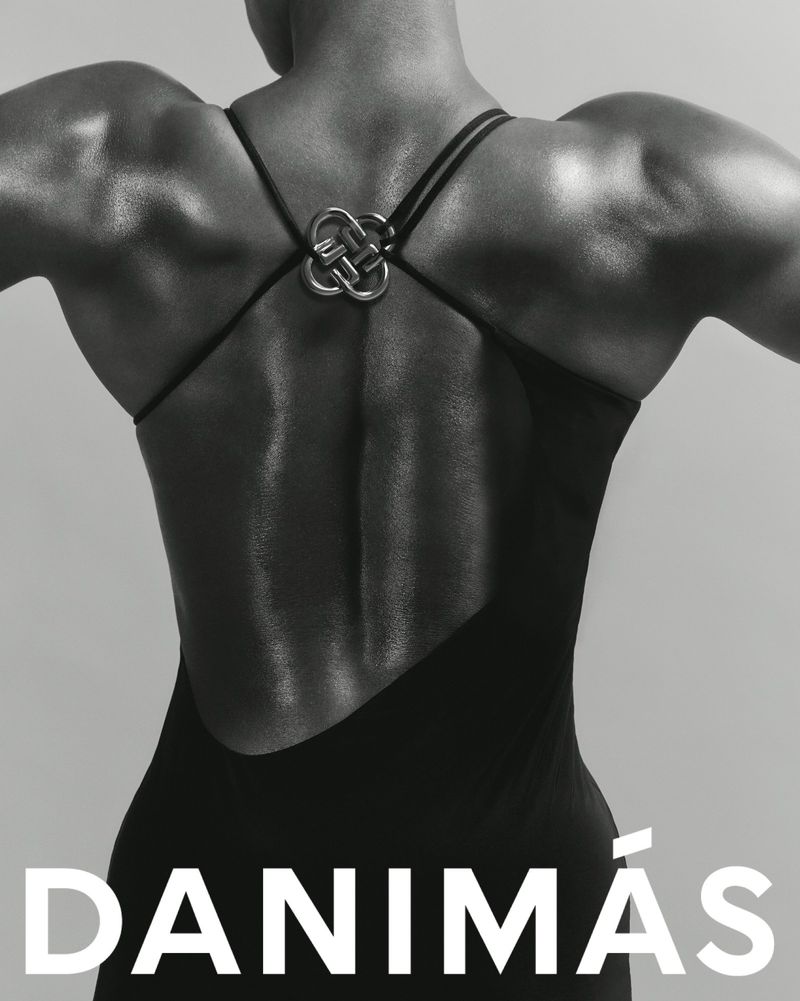 Woman's back in black dress with unique strap detail, monochrome fashion shot. Highlighting the dress design and musculature, studio setting.