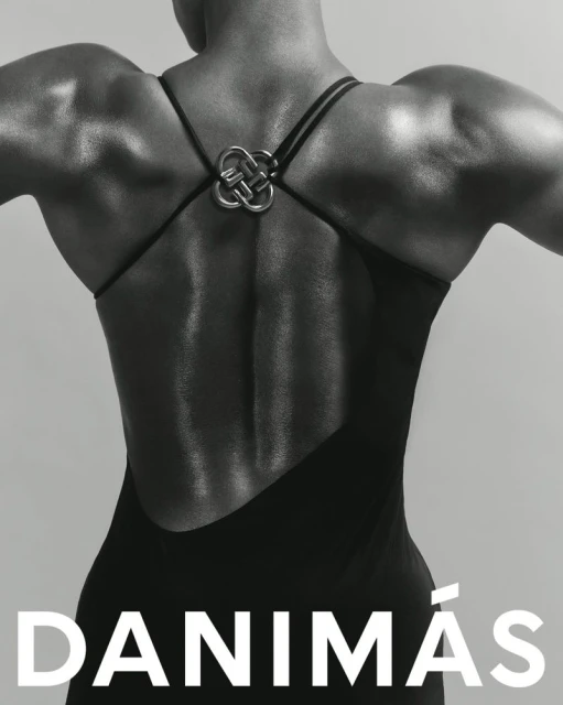Woman's back in black dress with unique strap detail, monochrome fashion shot. Highlighting the dress design and musculature, studio setting.