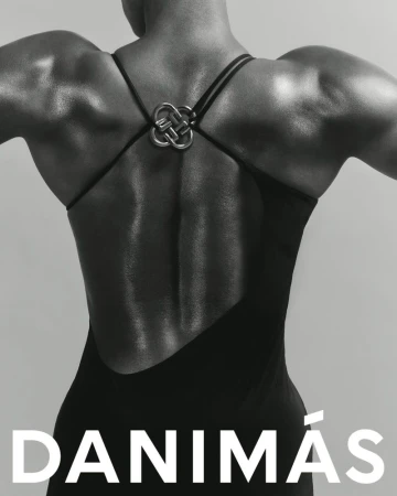 Woman's back in black dress with unique strap detail, monochrome fashion shot. Highlighting the dress design and musculature, studio setting.