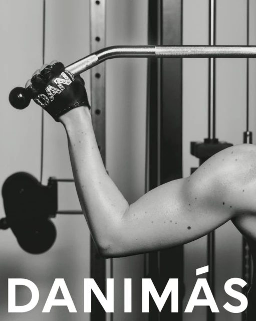Monochrome shot of a muscular arm pulling down on a lat pulldown machine in a fitness studio. Focus on strength and workout.