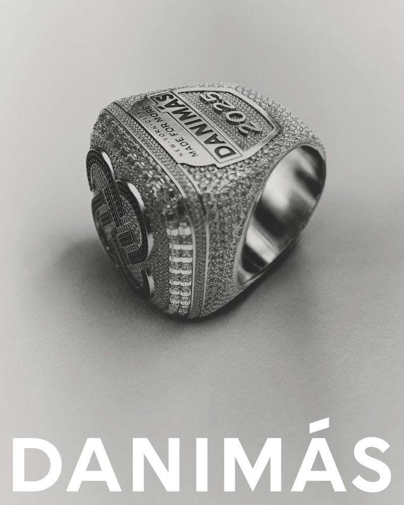 Monochrome product shot of a large embellished championship ring featuring encrusted stones and stamped text against a plain background