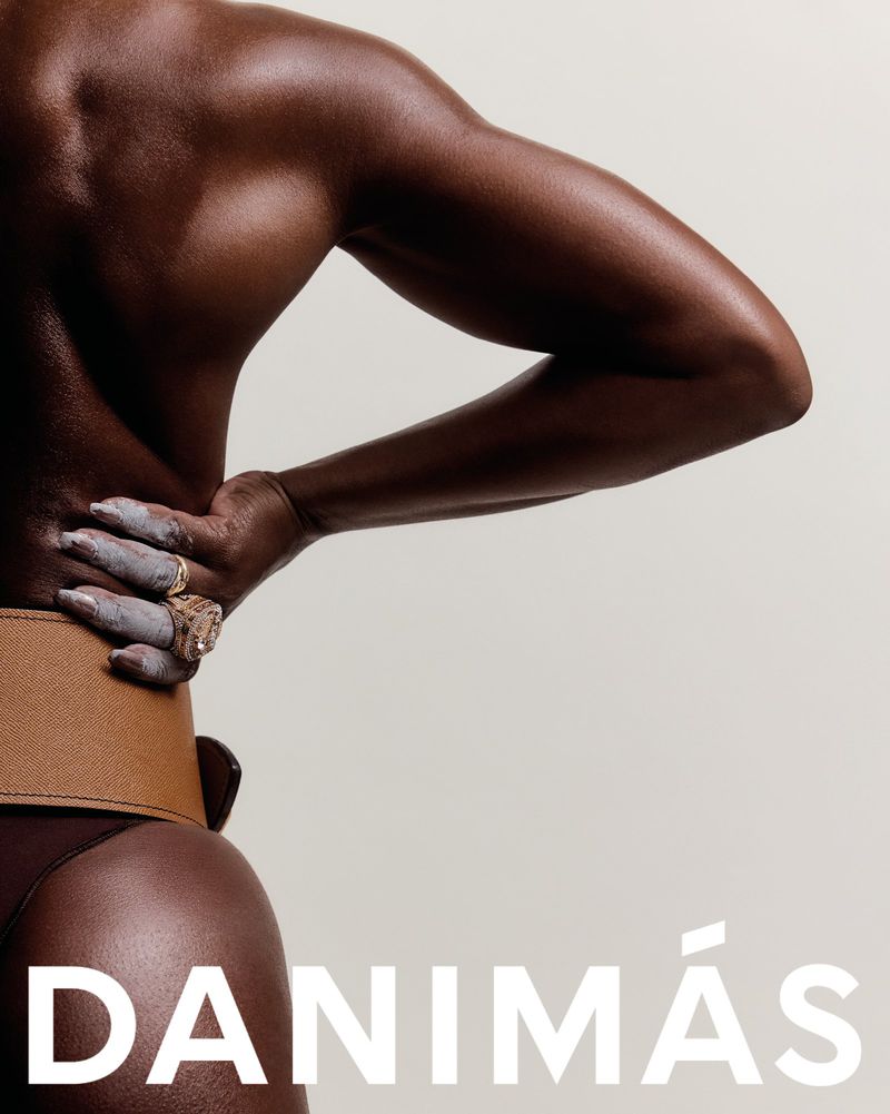 Back view of dark-skinned model wearing a brown belt and dark bottoms, posing against an off-white background with "DANIMÁS" text.