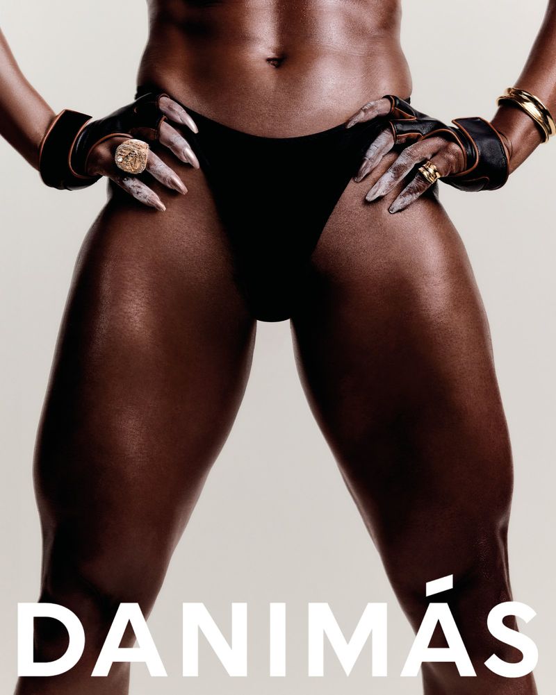Close-up studio shot of an adult female with dark skin wearing a black swimsuit bottom and gold jewellery. Muscular thighs are in focus.