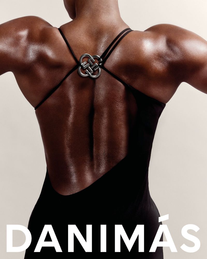 An adult woman's back is captured in a close-up studio shot, showcasing her bare skin, dress straps, and a decorative metal piece.