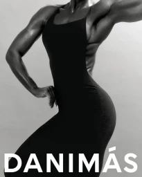 Close-up monochrome portrait of a muscular woman wearing a black athletic dress against a grey studio backdrop.