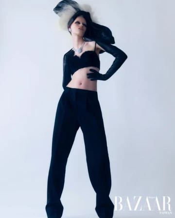 A stylish fashion photo features a woman in a black outfit with long gloves, posing against a bright background, wearing a unique feathered hat.