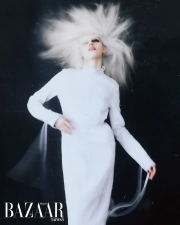 Fashion photo featuring a slender adult model with unique white hairstyle and makeup, wearing a white dress against a dark backdrop.