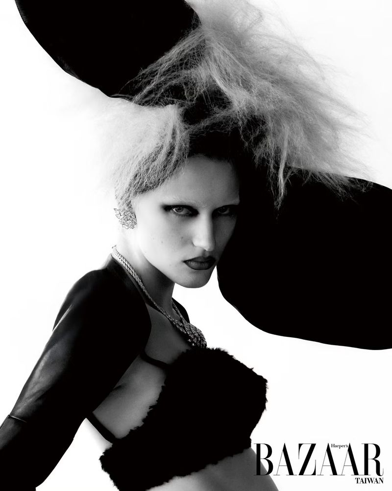 Black and white close-up fashion shot of a woman with distinctive hair, heavy makeup, statement jewelry, and avant-garde clothing.