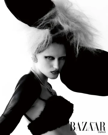 Black and white close-up fashion shot of a woman with distinctive hair, heavy makeup, statement jewelry, and avant-garde clothing.